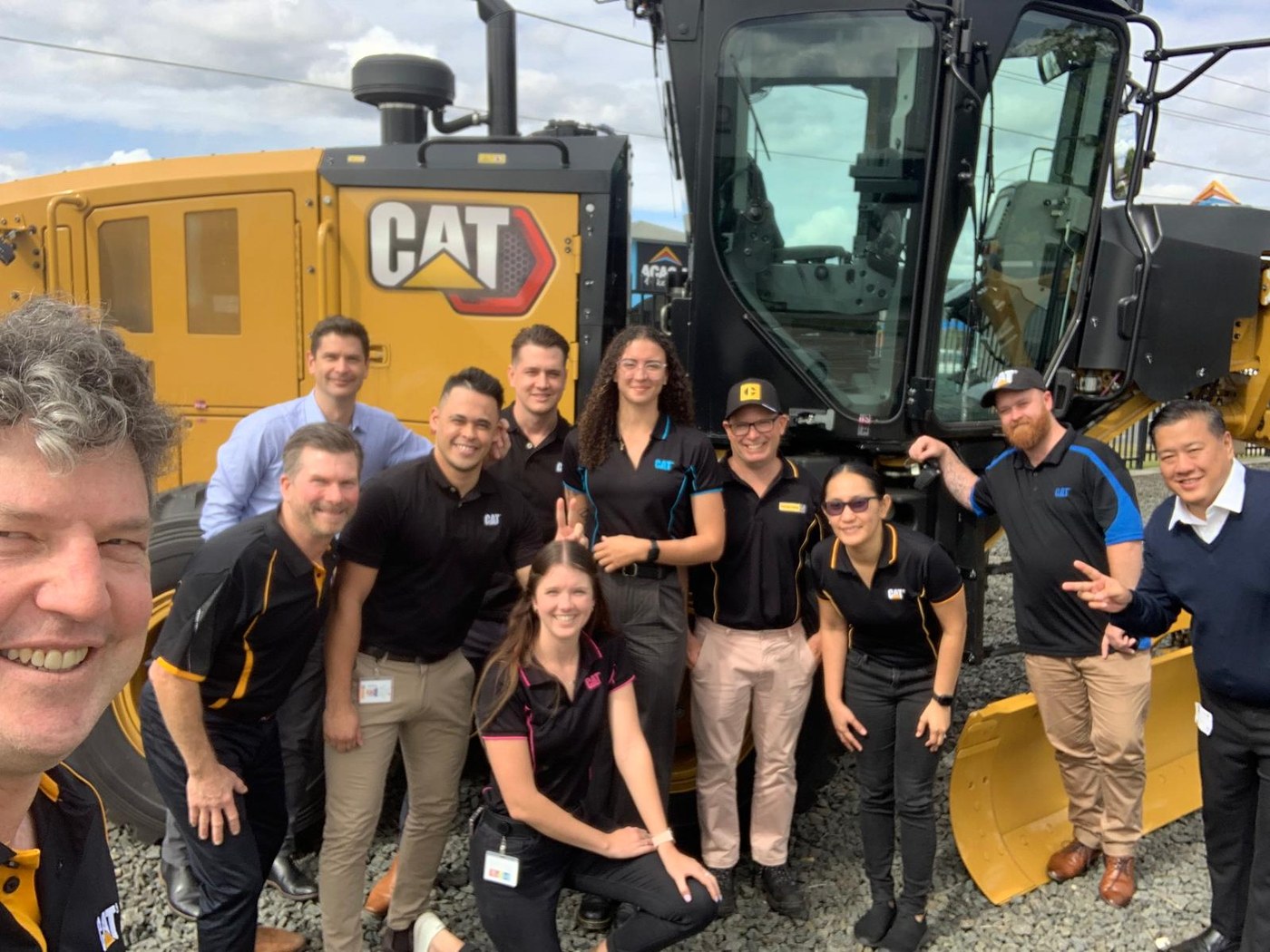 Aftermarket Inside Sales team in Brisbane, Australia, beside a Caterpillar grader